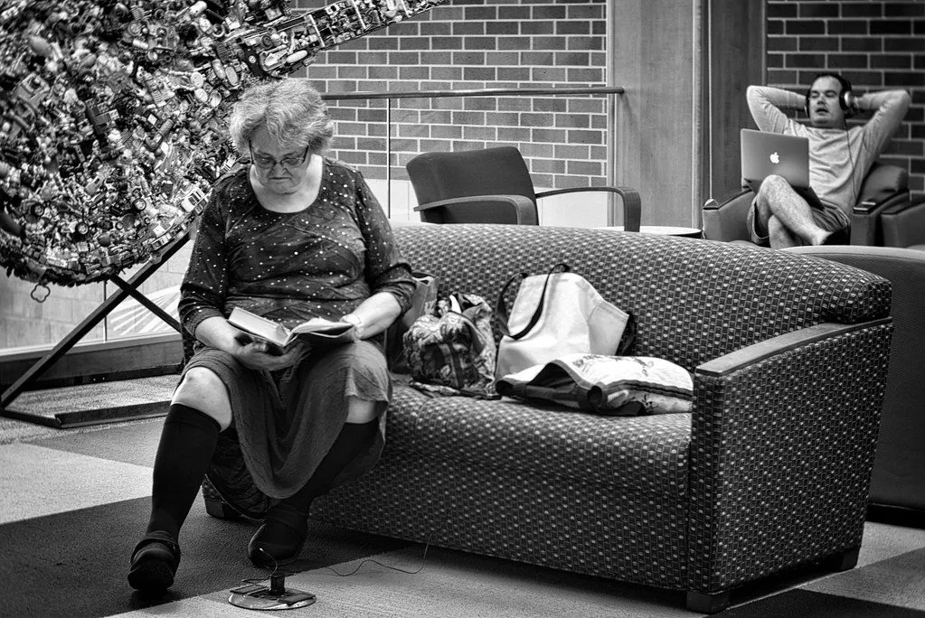 elderly woman reading a book at a table